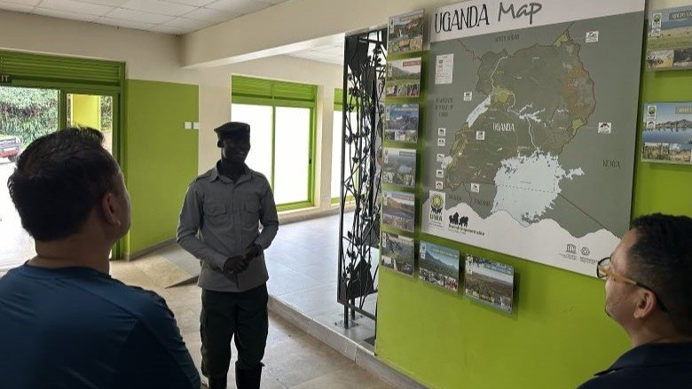Two delegates from Bhutan receiving a presentation from a member of the Uganda Wildlife Authority in front of a map of Uganda